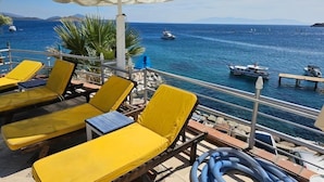 A deck with yellow lounge chairs and a white umbrella, overlooking a body of water with boats. - portofino hotel (Bodrum)