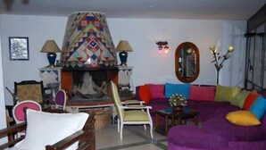 A living room with a colorful fireplace, a purple sofa, and a wooden chair. - portofino hotel (Bodrum)