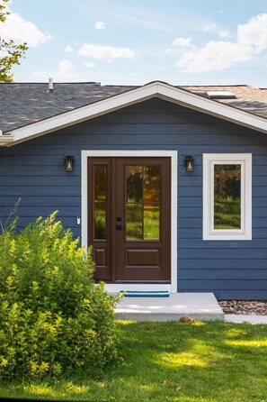 A house with a dark blue exterior, a brown front door with glass panels, and a small porch with a white railing.