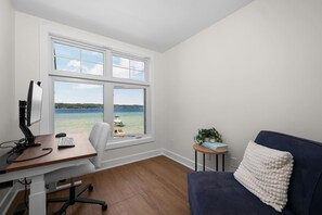 Una habitación con escritorio, computadora y vista a un cuerpo de agua a través de amplias ventanas.