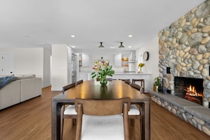 Una cocina moderna con armarios blancos, una chimenea de piedra y un comedor con mesa y sillas de madera.