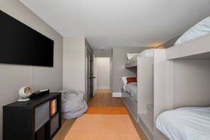 A modern bedroom with bunk beds, a flat-screen TV, a desk with a lamp, and a bookshelf.