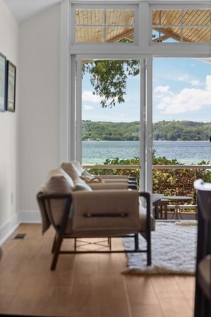 Habitación con un gran ventanal corredera que da a una vista de lago, un sofá y una pequeña mesa.