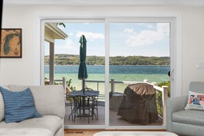 Ein Zimmer mit einer Schiebetür zu einem Balkon, auf dem sich ein Tisch, Stühle, ein Grill und ein Blick auf einen See und Hügel liegen.