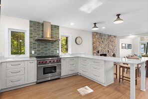 A modern kitchen with white cabinetry, a built-in oven, a gas range, and a stone accent wall.