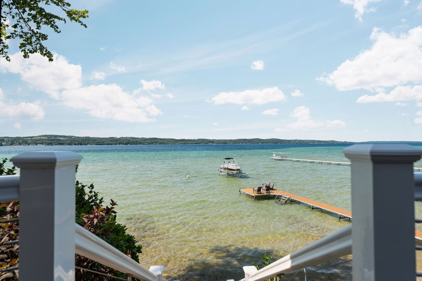 A clear view of a lake with a dock and a boat, surrounded by greenery and a distant shoreline.