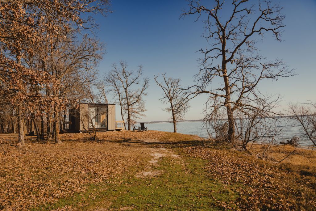 A cabin by a lake with a clear path leading to it, surrounded by leaf-covered ground and trees.