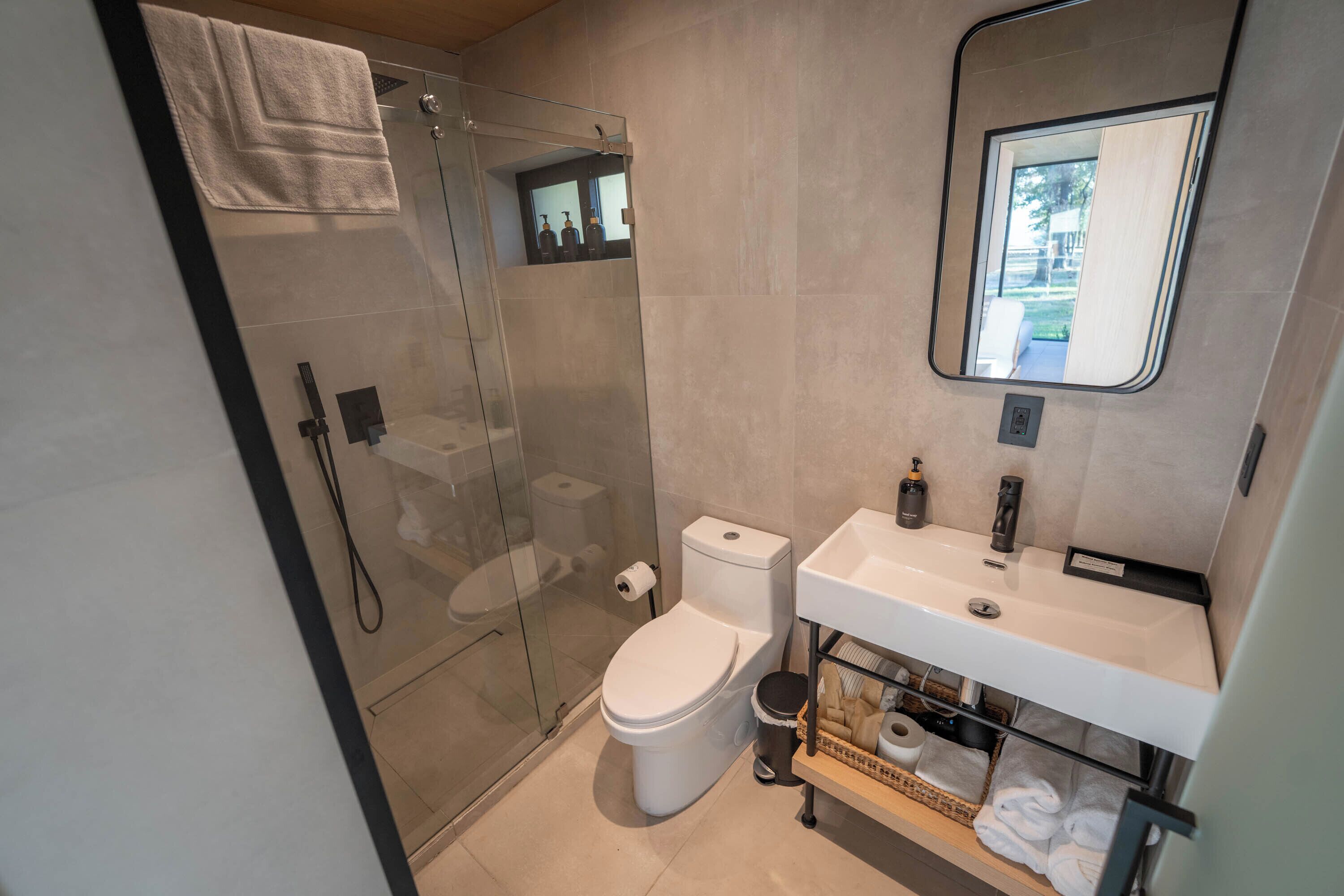 A modern bathroom with a glass shower enclosure, a toilet, a sink with a mirror, and a towel rack.