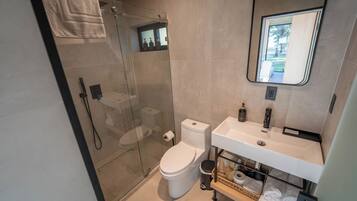 A modern bathroom with a glass shower enclosure, a toilet, a sink with a mirror, and a towel rack.