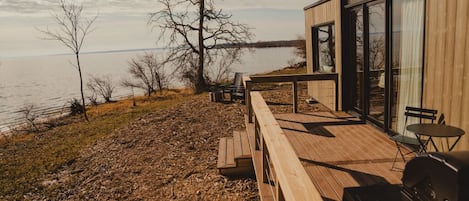 Eine Holzterrasse mit Grill, Tisch und Stühlen mit Blick auf ein Gewässer.