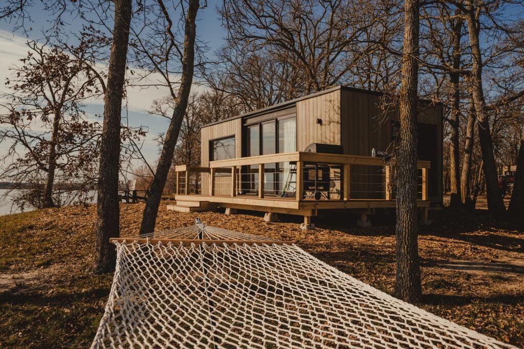 A modern wooden cabin by a lake with a hammock and a deck.