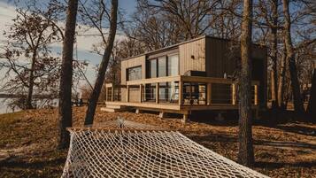 A modern wooden cabin by a lake with a hammock and a deck.