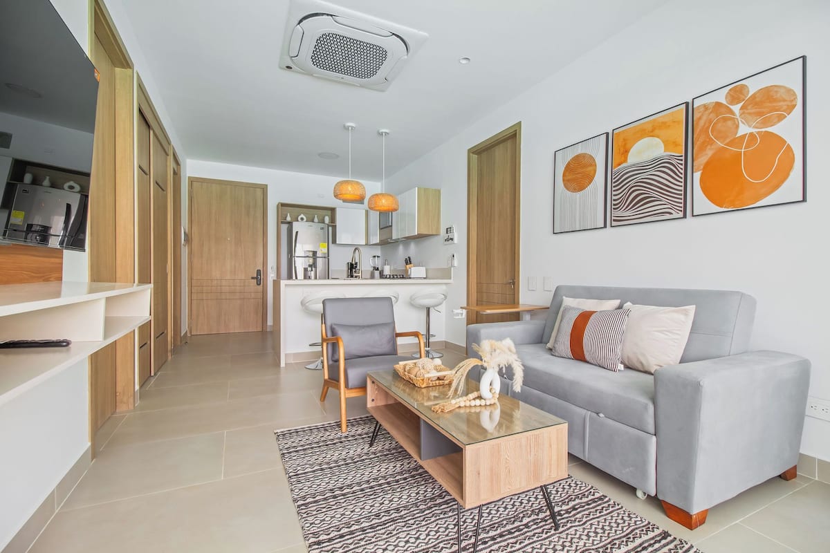 A modern living room with a grey sofa, a coffee table, and a kitchen in the background.