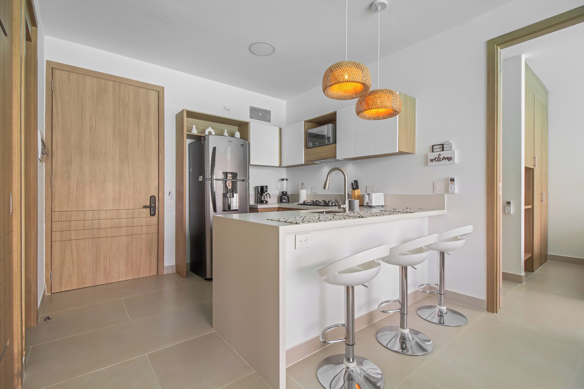 Een moderne keuken met een centraal eiland, roestvrijstalen apparatuur en een bord met de tekst 'welcome' aan de muur.