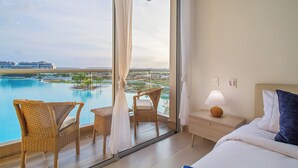 Een hotelkamer met een groot balkon, zwembadzicht en een bed met nachtkastje.