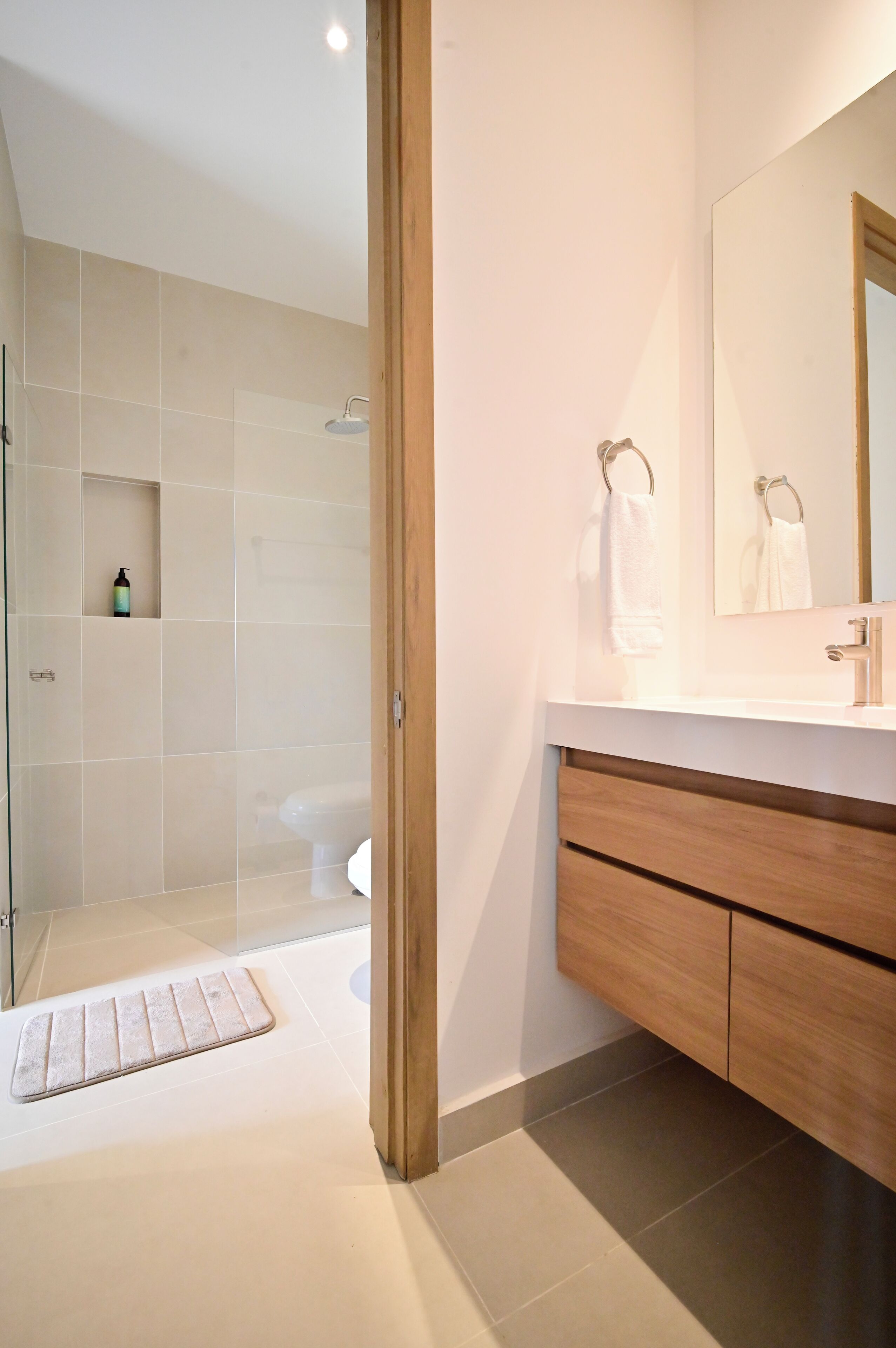 A modern bathroom with a glass shower enclosure, a white sink, and wooden cabinetry.
