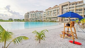Een resort met een groot zwembad, een zandstrand en een meerlaags gebouw met balkons.