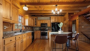 Een houten keuken in cottage-stijl met granieten aanrechtbladen, roestvrijstalen apparatuur en een centraal kookeiland met barstoelen.