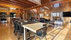 Een ruim houten blokhutinterieur met een grote eettafel, een keukenhoek en een gezellige woonkamer.
