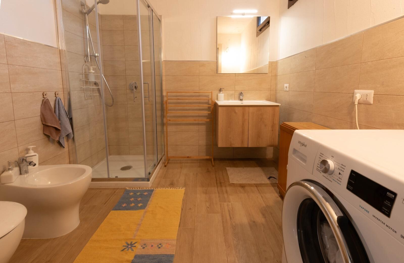 Un baño moderno con mampara de vidrio, lavabo empotrado, inodoro y lavadora de carga frontal.