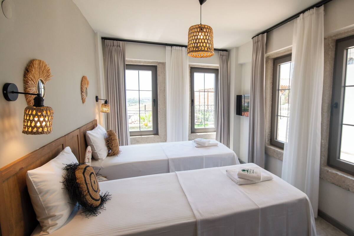 Habitación de hotel con dos camas, televisor y ventanas amplias con cortinas.