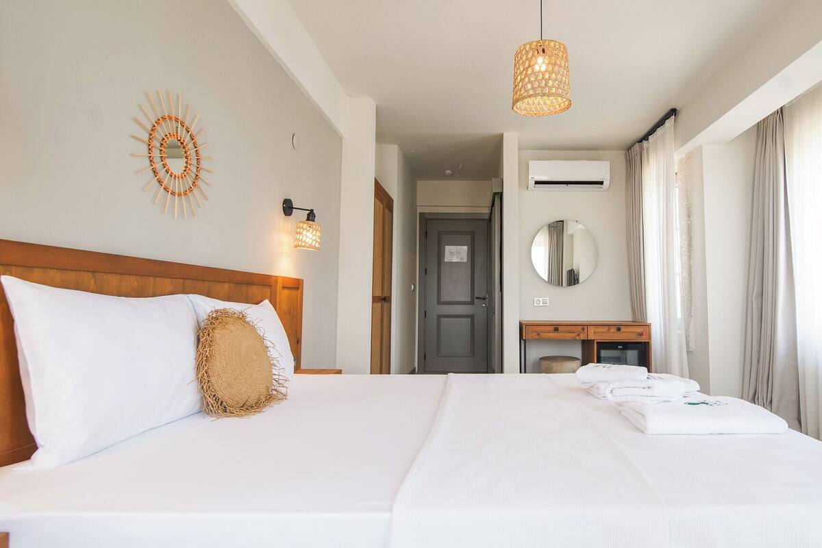 Una habitación de hotel con una cama grande, un cabecero de madera, un espejo adosado a la pared y una lámpara colgante.