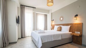 Quarto de hotel com uma cama grande, cabeceira de madeira, mesa de cabeceira com abajur e televisão fixada na parede.