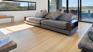 A modern living room with a grey sofa, wooden coffee table, and a large window offering a view of the outdoors.