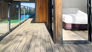 A modern bedroom with a large bed, a wooden floor, and a balcony with glass railings.