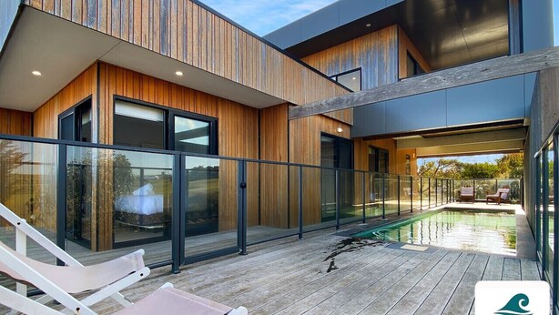 A modern building with a wooden exterior, large glass windows, and a pool area with lounge chairs.