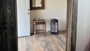 Um quarto com porta de madeira, um espelho, uma mesa pequena, um aquecedor e um ventilador de teto.