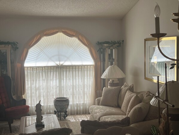 A living room with a sofa, a coffee table, a lamp, and a large window with curtains.