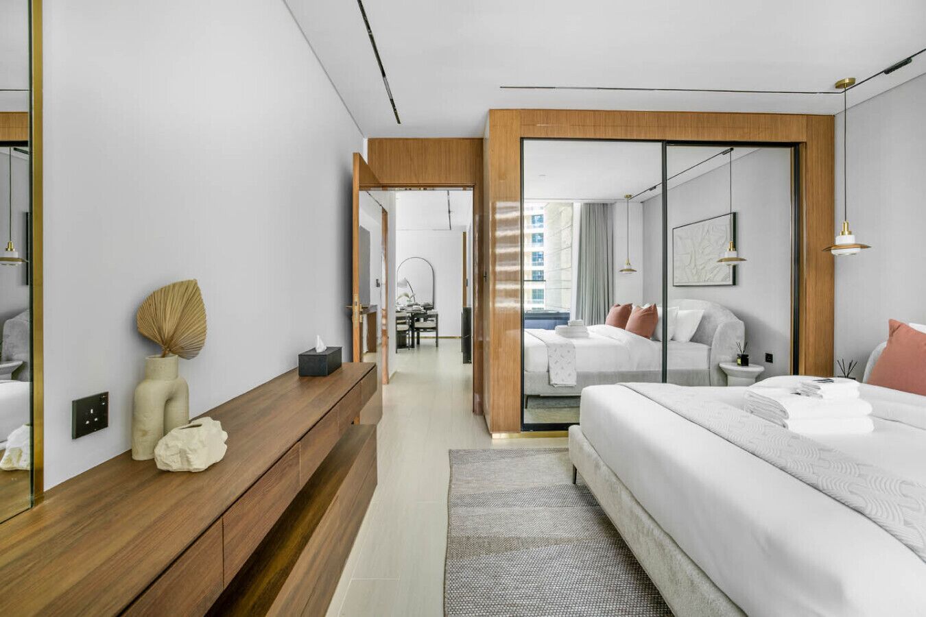 Une chambre d’hôtel moderne avec un grand lit, un banc en bois, un miroir et une vue sur la ville, visible à travers une porte vitrée.