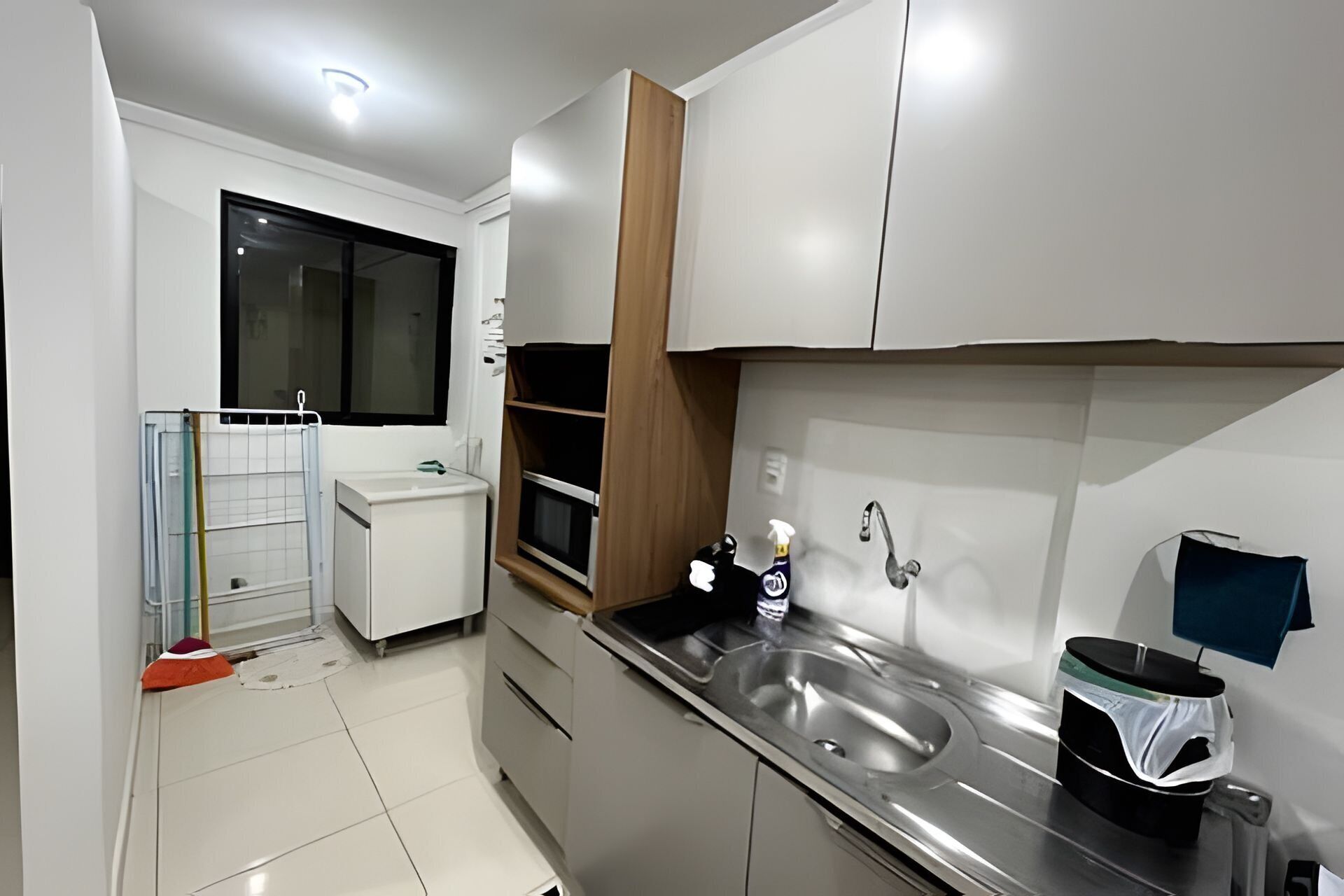 A modern kitchen with a stainless steel sink, a microwave, and a window with blinds.