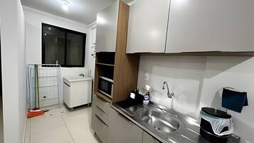 A modern kitchen with a stainless steel sink, a microwave, and a window with blinds.