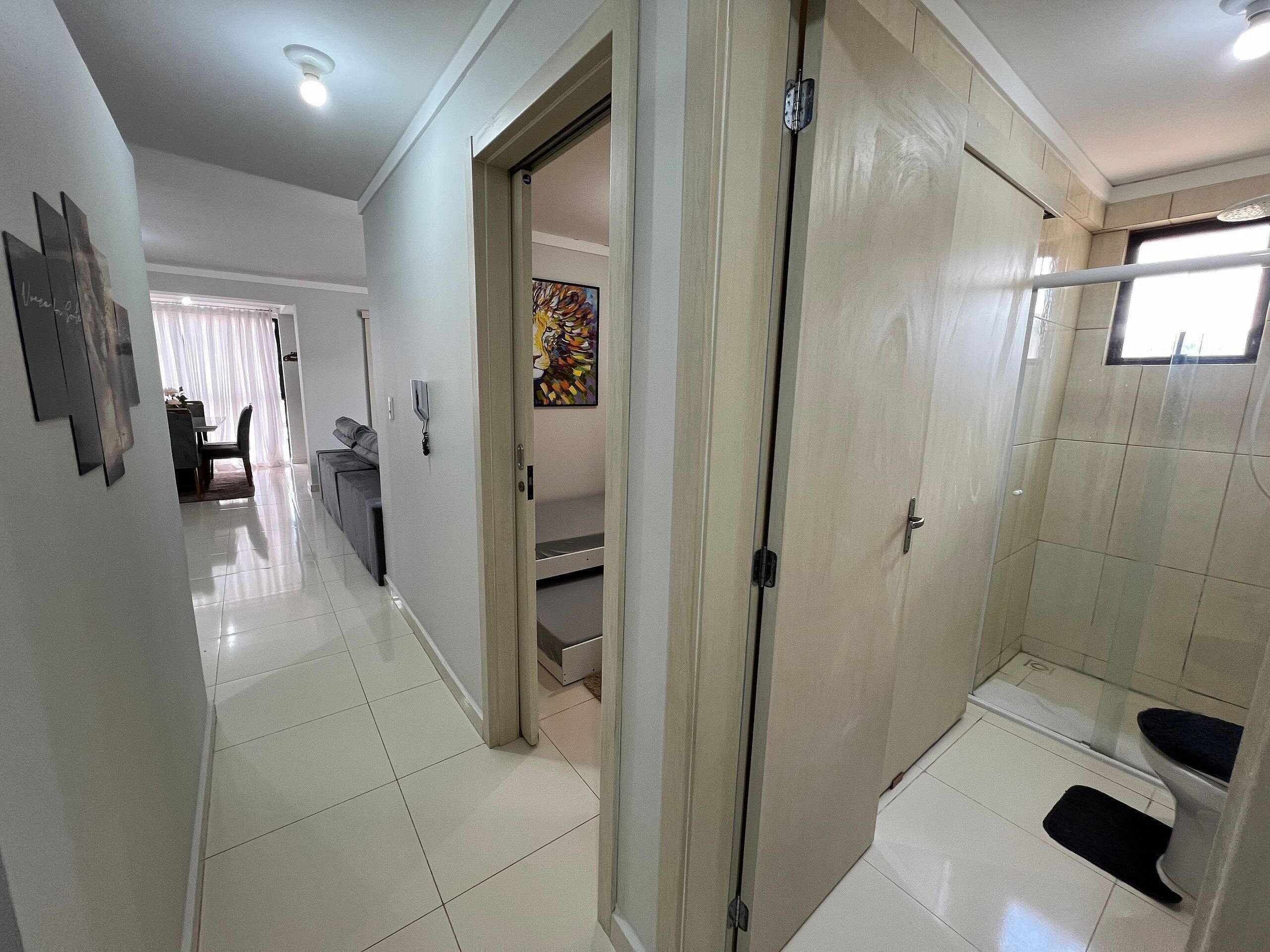 A hotel room with a shower, a door leading to a bathroom, and a hallway with a dining area.
