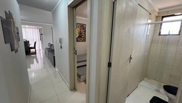 A hotel room with a shower, a door leading to a bathroom, and a hallway with a dining area.