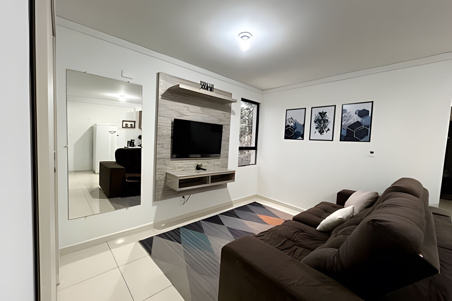 Una sala de estar con televisión de pantalla plana, un sofá, una mesita de centro y un tapete estampado.