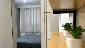 Ein gemütlicher Raum mit einem Bett, einem kleinen Tisch mit Topfpflanzen und einem fensterartigen Bereich, der mit einem Vorhang verziert ist.