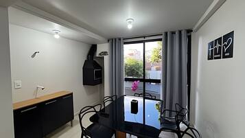 Un comedor compacto con una mesa y sillas, un horno empotrado, una ventana con cortinas y vistas al exterior.