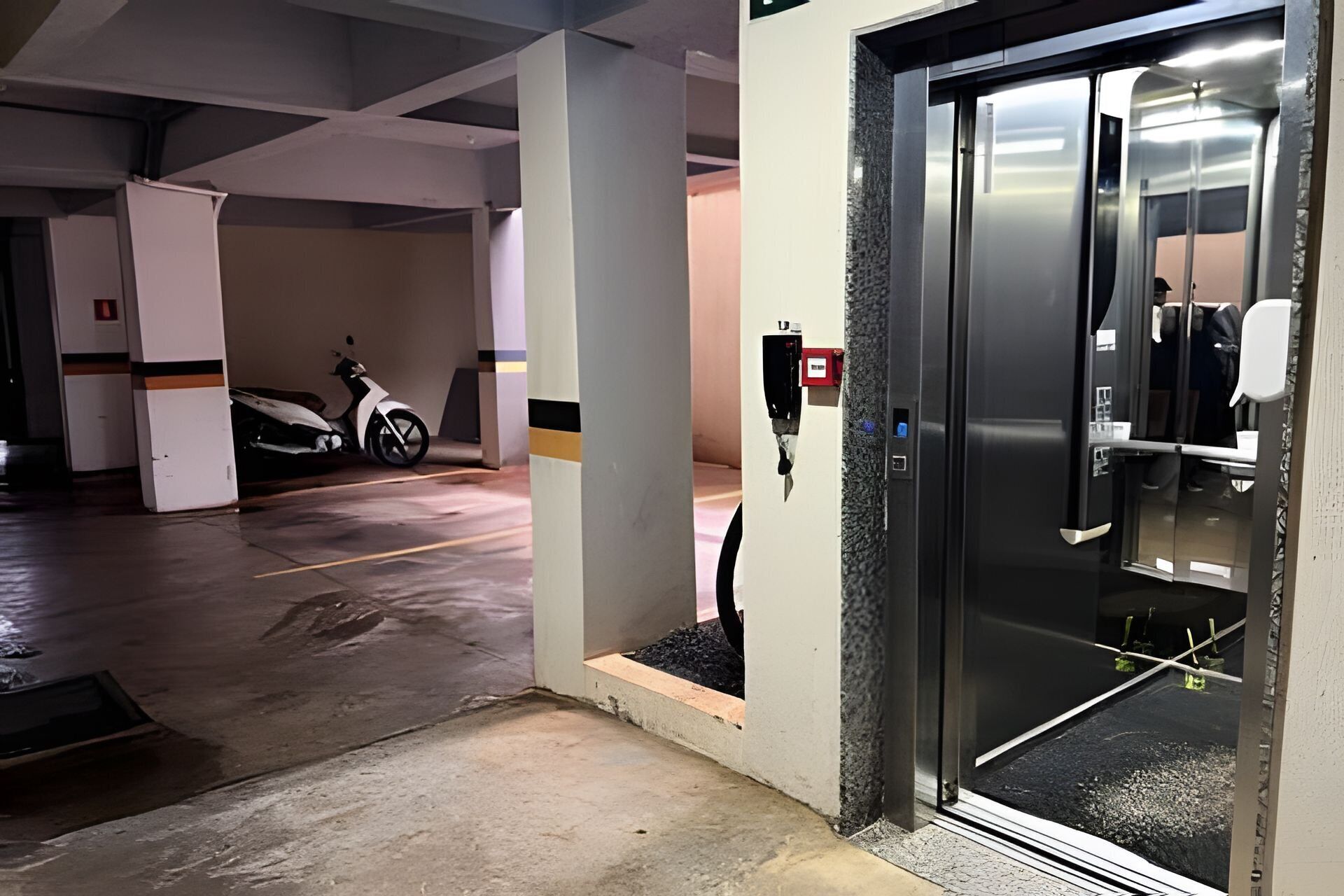 A parking garage with a scooter, a fire alarm, and a door to a building.