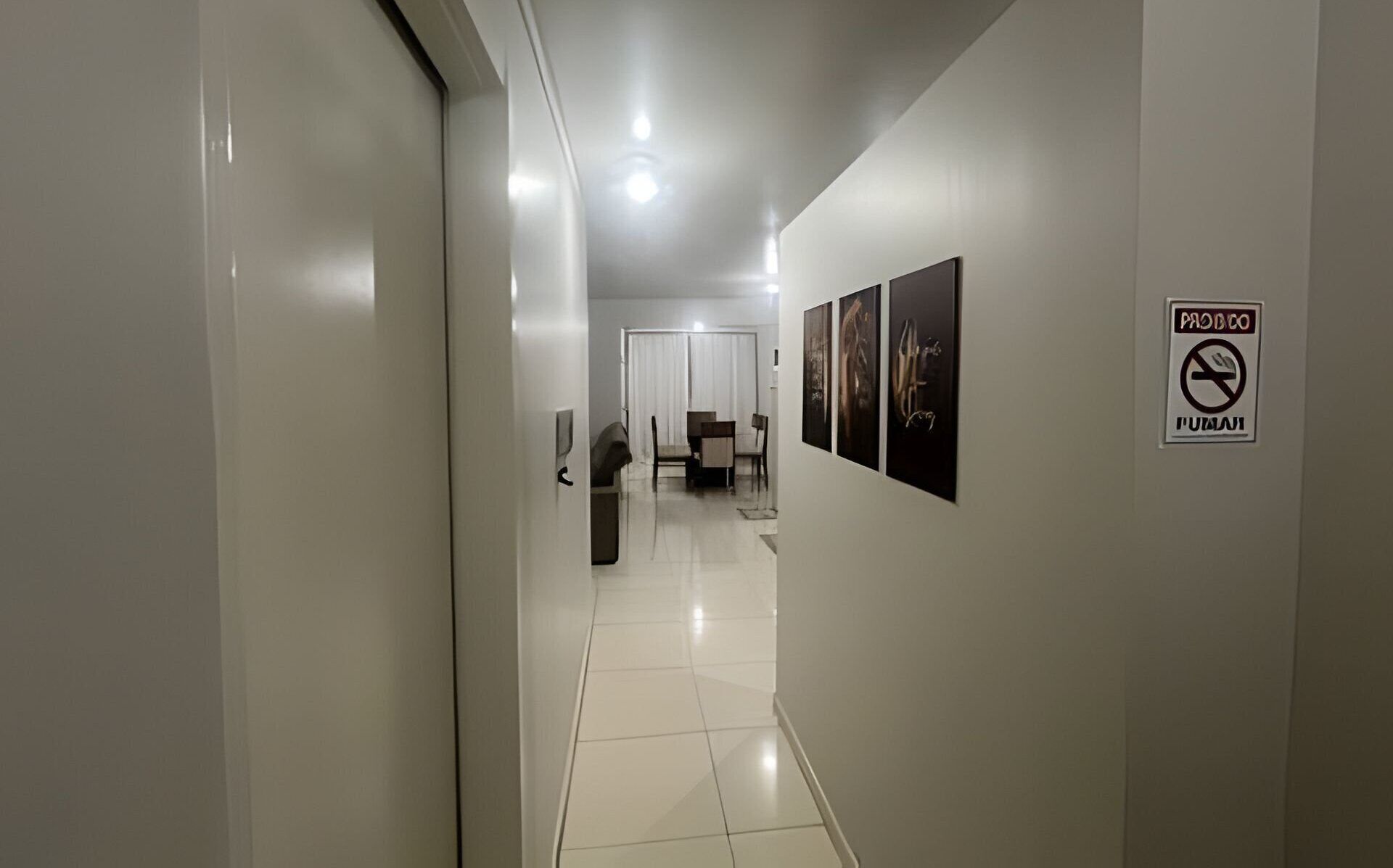 Um corredor com área de jantar, um aviso de 'Não Fumar' e obras de arte nas paredes.