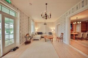 A spacious living room with a large sofa, a round coffee table, and a dining area with wooden furniture.