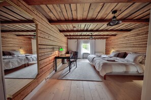 A room with wooden walls and ceiling, two beds, a desk with a chair, and a window with curtains.