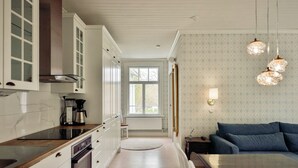 Eine moderne Küche mit weißen Schränken, einem Einbauofen und einer Kaffeemaschine. Ein runder Teppich führt zu einem Fenster, und es gibt ein blaues Sofa mit einer Wandlampe.