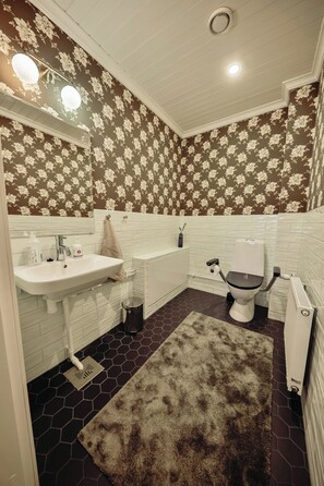 A bathroom with a white sink, toilet, and bathtub, featuring floral wallpaper and a hexagonal patterned floor.