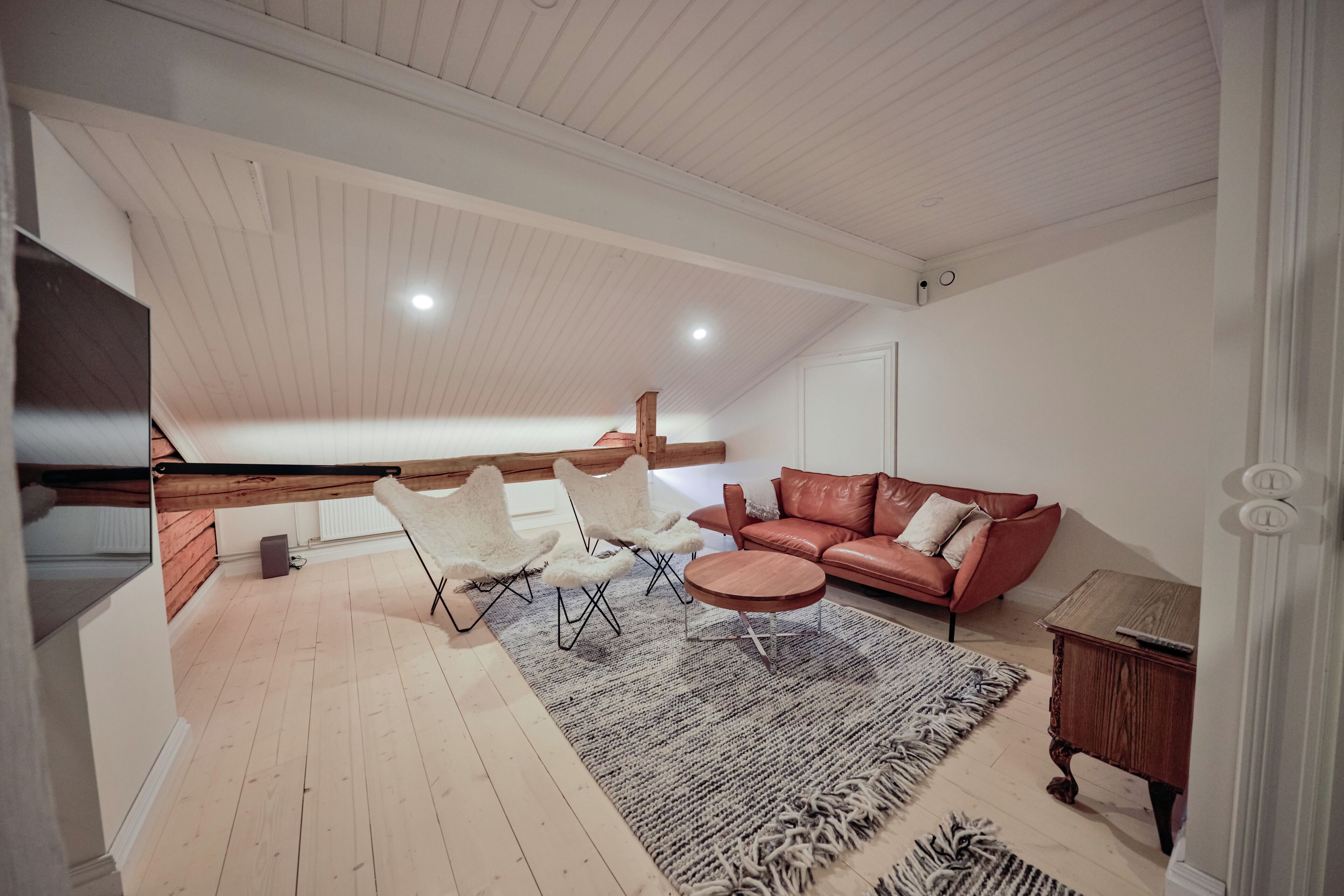 A spacious loft with a high ceiling, a cozy seating area with a leather sofa and white chairs, a wooden dining table, and a large rug.