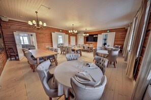 A spacious dining area with multiple tables and chairs, wooden paneling on the walls, and a chandelier.