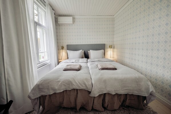 A double bed with a grey headboard, two bedside tables with lamps, and a window with curtains.