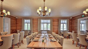 Ein geräumiger Speisesaal mit einem langen Holztisch, der für eine Mahlzeit gedeckt ist, umgeben von gepolsterten Stühlen.